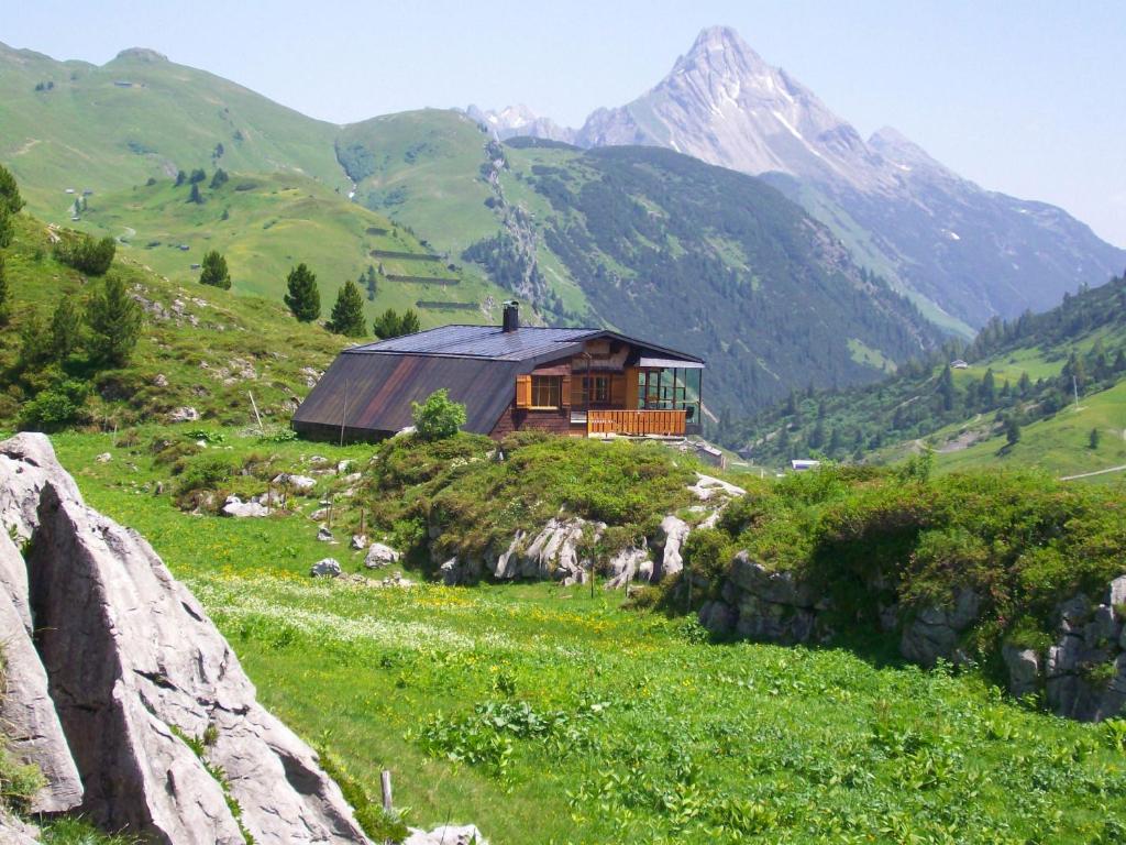 una casa en una colina con montañas en el fondo en Pfefferkornhütte, en Warth am Arlberg