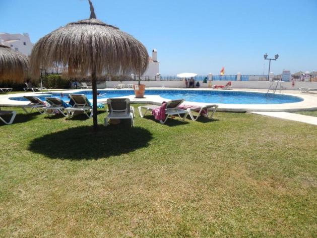 eine Gruppe von Stühlen und einem Sonnenschirm neben einem Pool in der Unterkunft Casa Frijo Tropicana in Nerja