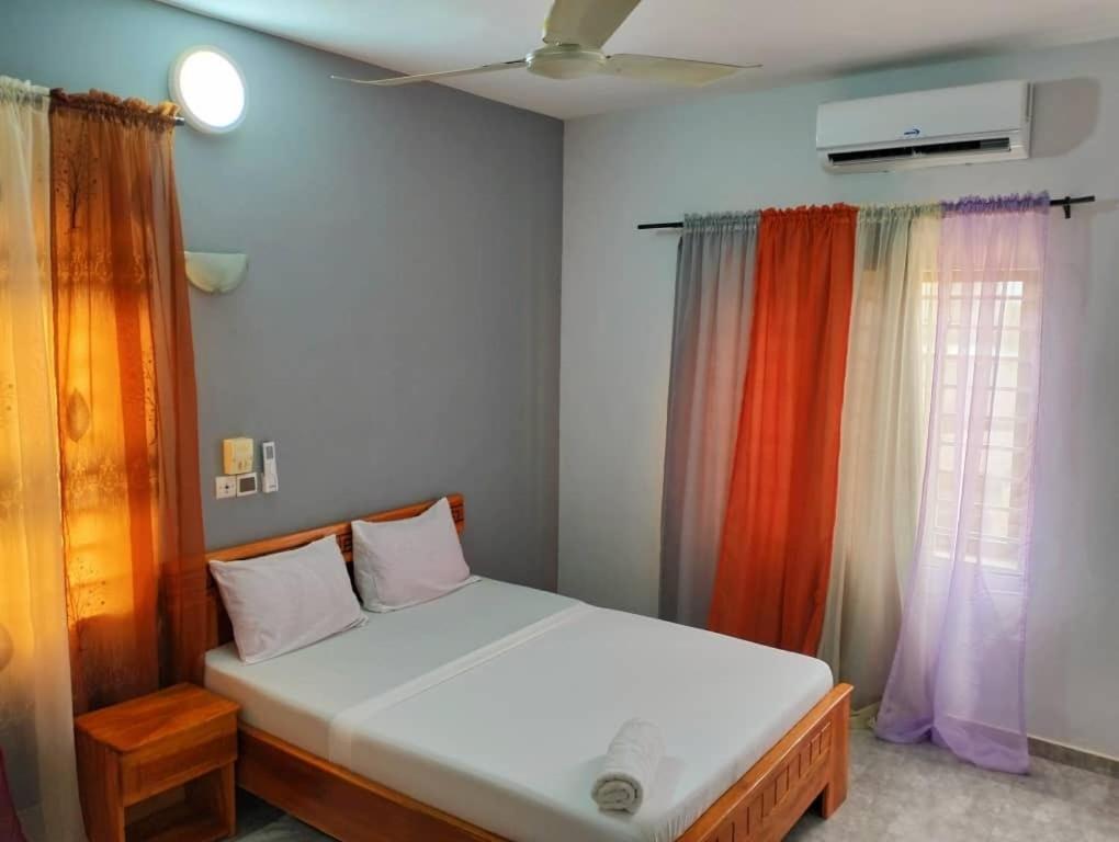 Cama en habitación con cortinas de arco iris en Chez Gero, en Cotonou