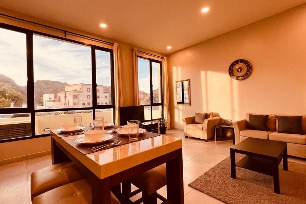 een woonkamer met een tafel en een groot raam bij ONE 2BHK Apartments in Muscat