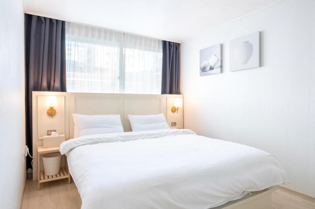 a white bedroom with a large bed and a window at Le Cocon Seoul in Seoul