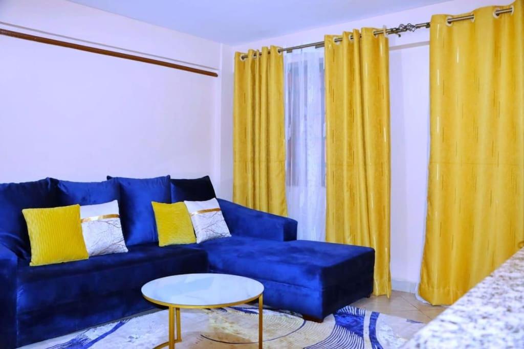 een blauwe bank in een woonkamer met gele gordijnen bij A cosy and spacious one bedroom apartment in Ruaka