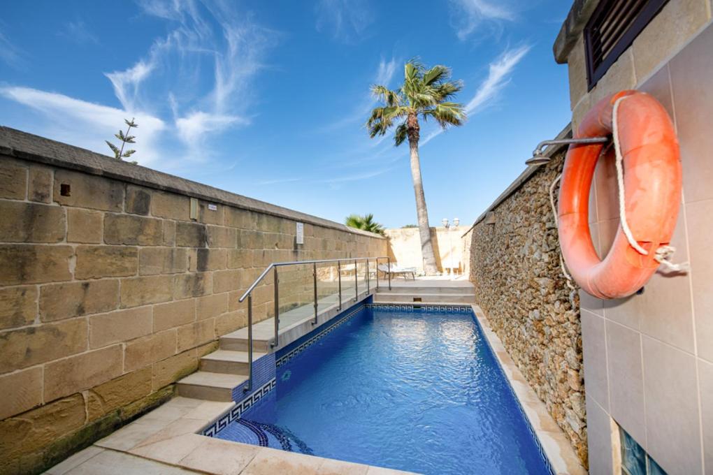 a swimming pool next to a wall with a palm tree at Ta' Rozi 5 Bedroom Farmhouse with Private Pool in Għarb