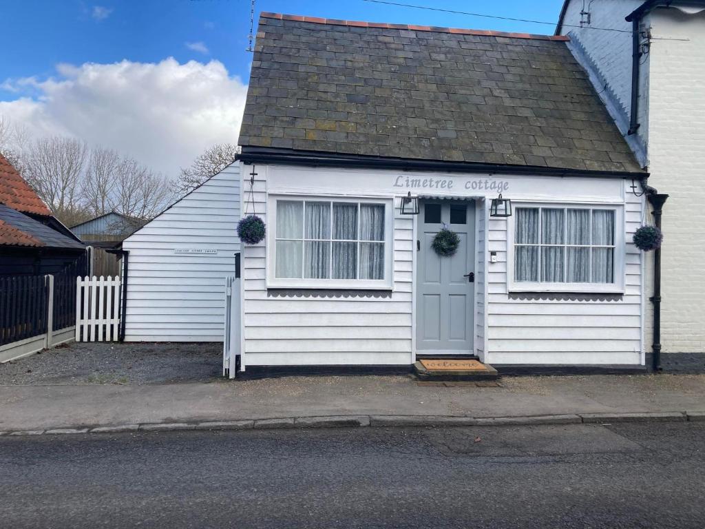 a white house with a door on a street at Lime Tree Cottage in Tillingham