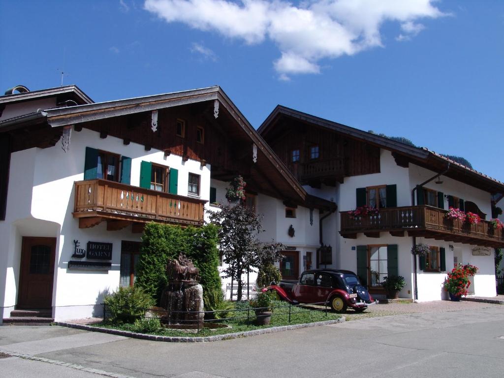a white building with wooden balconies and a car parked outside at Hotel Ferienhaus Fux in Oberammergau