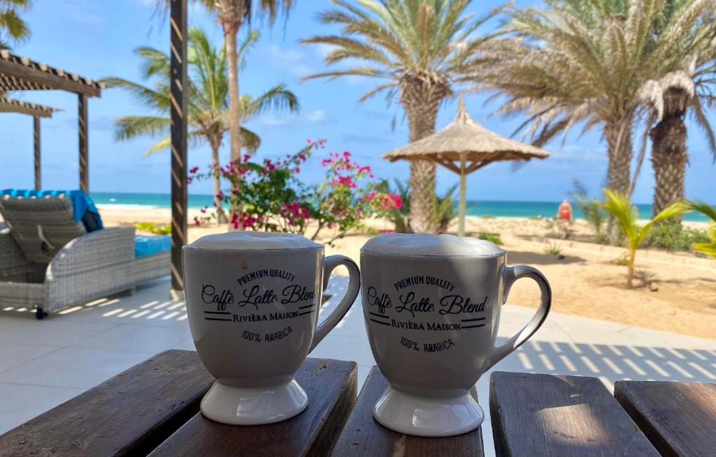 CabeçadasにあるVila Mare - Praia de Chaves frontlineのビーチのそばの木製テーブルに座ったコーヒーマグカップ2つ