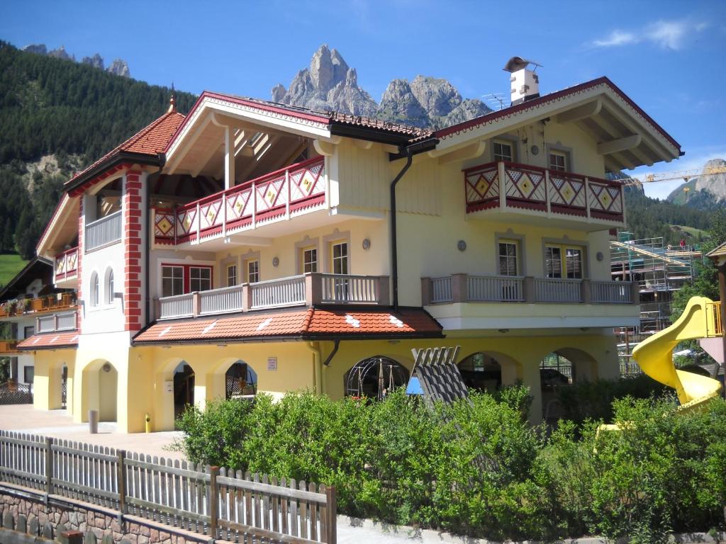 una grande casa gialla con montagne sullo sfondo di Casa Fior del Soreie a Pozza di Fassa