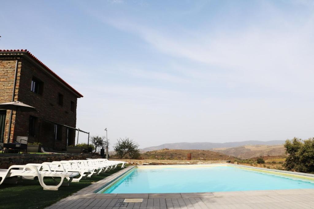 a swimming pool with white lounge chairs next to a building at Eira da Fraga in Vila Nova de Foz Coa