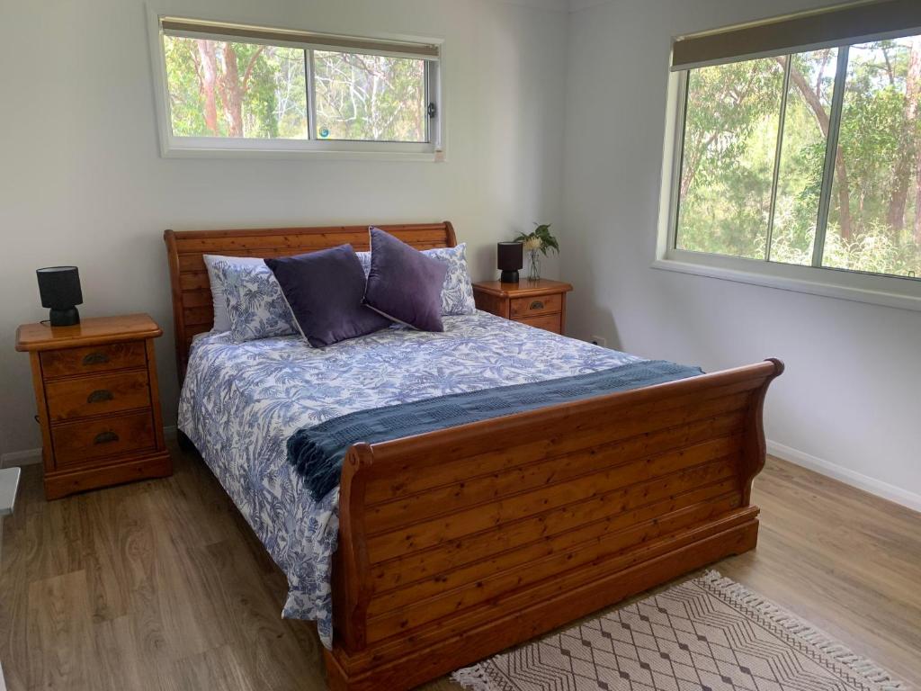 a bedroom with a wooden bed and two windows at Bush Beach Retreat in Caloundra