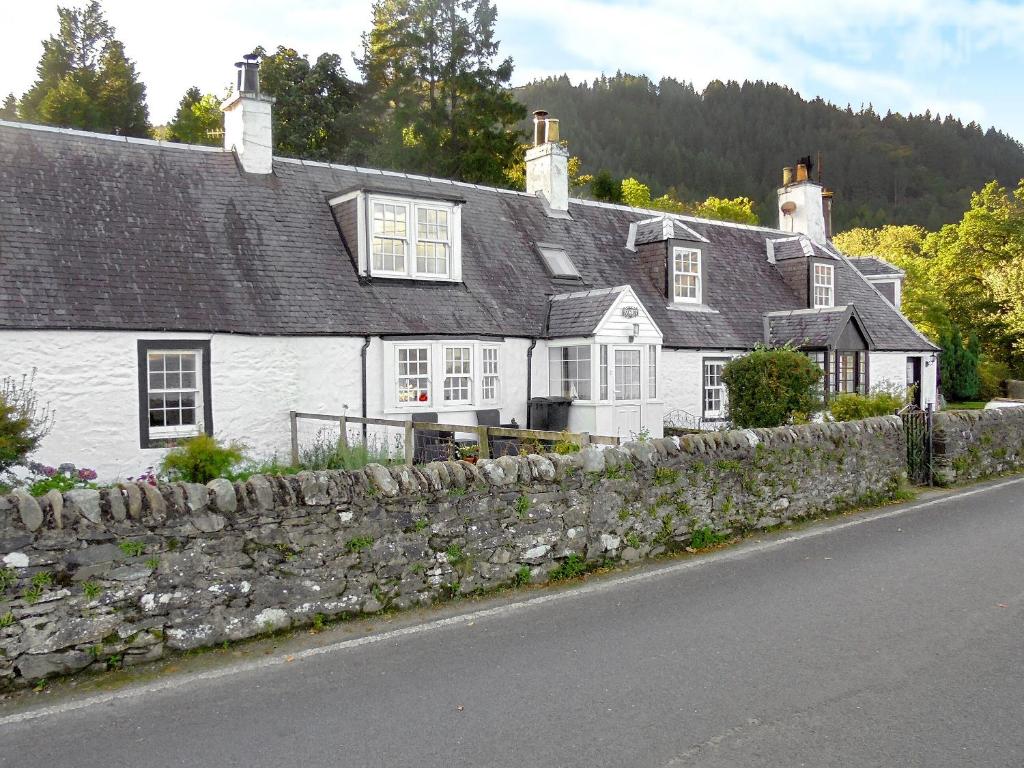 a white house with a stone wall next to a street at Raglan Cottage in Ardentinny