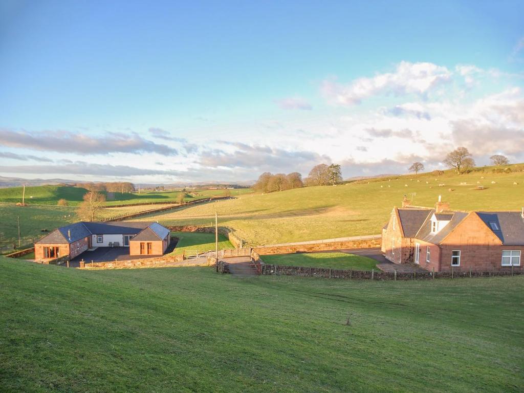 a group of houses on a green field with a hill at Liftingstane Farmhouse in Closeburn