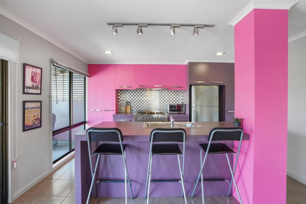a kitchen with pink walls and a bar with stools at Birdland in Port Fairy