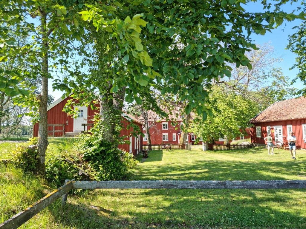 a red barn with a tree and a fence at Kobbar & Skär Vandrarhem in Ellös