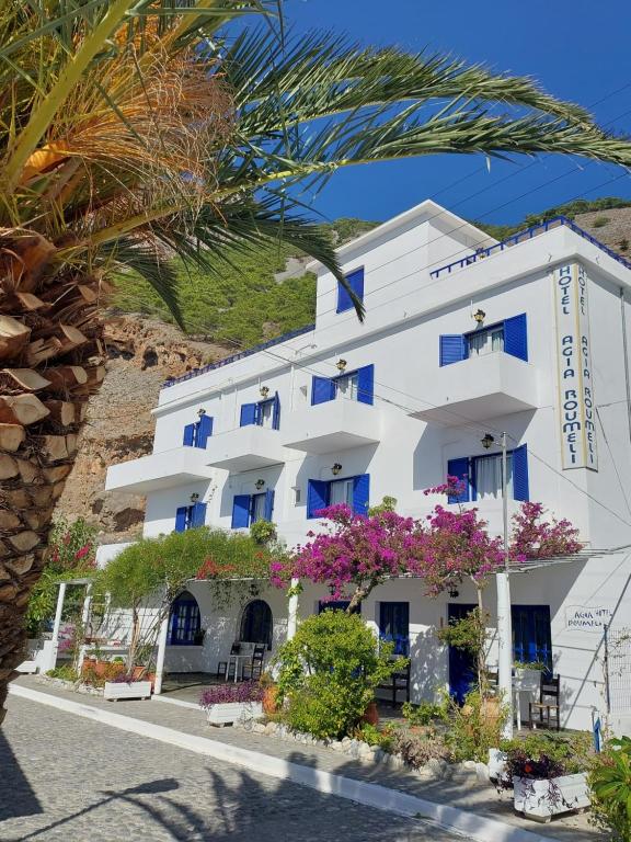 un edificio blanco con ventanas azules y flores en Agia Roumeli APARTMENT, en Agia Roumeli
