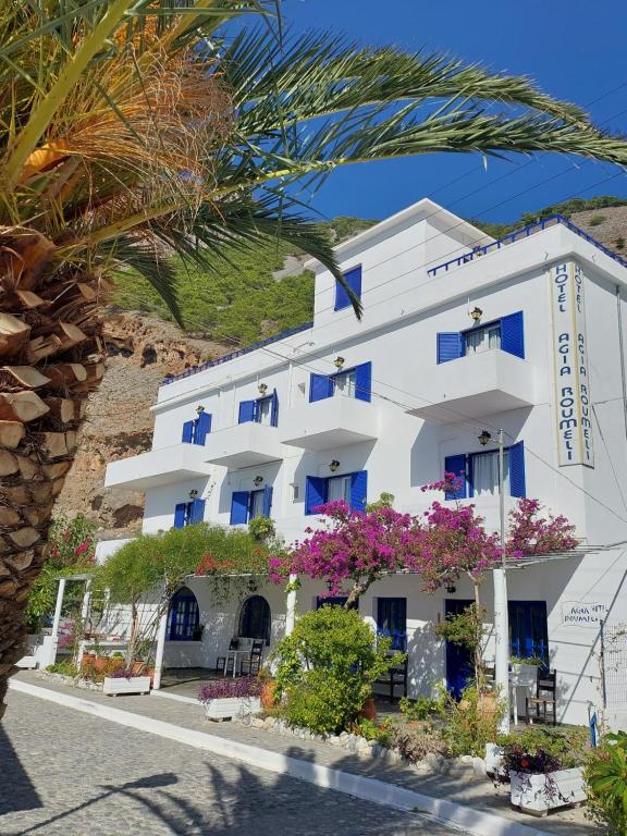 a white building with blue windows and flowers at Agia Roumeli APARTMENT in Agia Roumeli