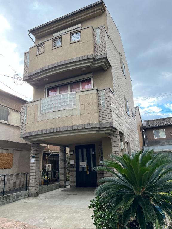 ein hohes Gebäude mit einem Baum davor in der Unterkunft Guest House Kubo Homes Matsu in Osaka