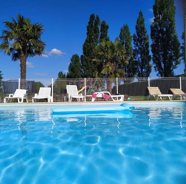 a swimming pool with blue water and chairs and palm trees at Chambre d'hôte Manoir de La Baudonnière in Monsireigne