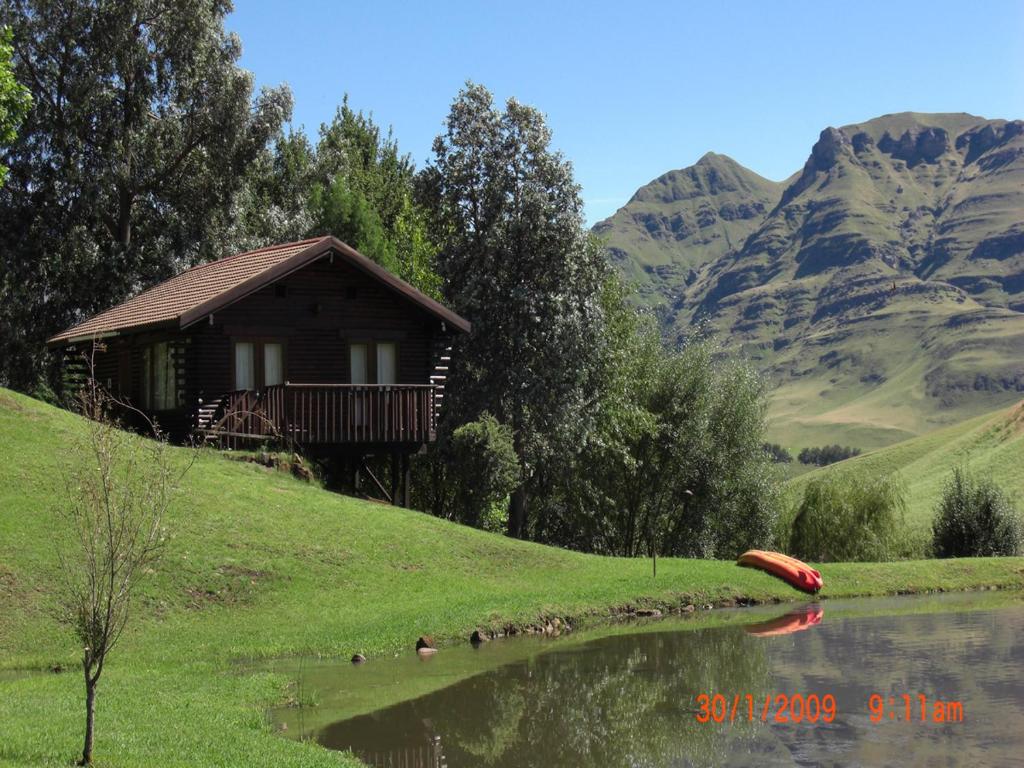 a small cabin on a hill next to a lake at Eland Valley Resort in Underberg