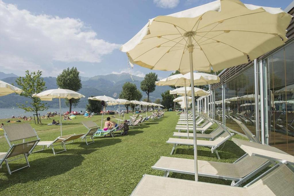 een rij witte stoelen en parasols op een strand bij Seven Park Hotel Lake Como - Adults Only in Colico