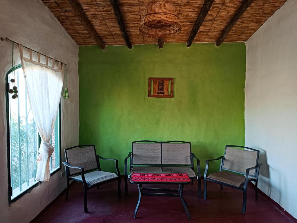 drie stoelen en een tafel in een kamer met een groene muur bij Huerta Las Señoritas in Senador Pérez