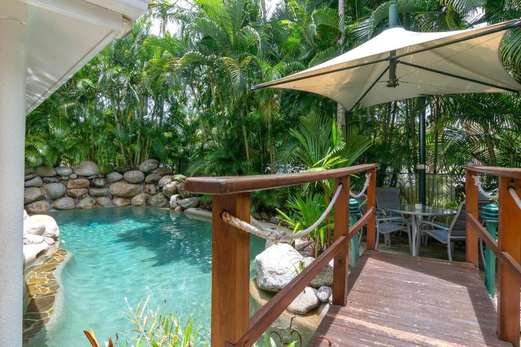 a pool with an umbrella next to a wooden deck at Seascape Holidays - Coral Apartments in Port Douglas