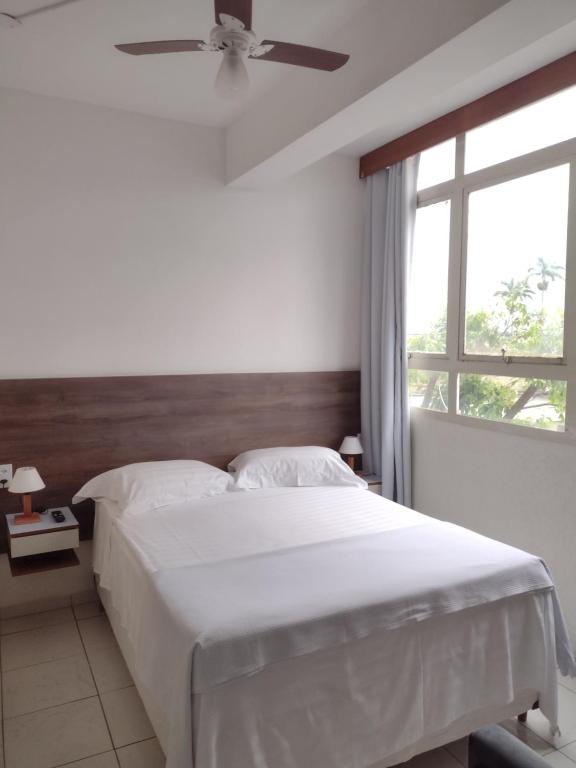 um quarto com uma cama, uma ventoinha de tecto e uma janela em Studio no Centro em Araxá
