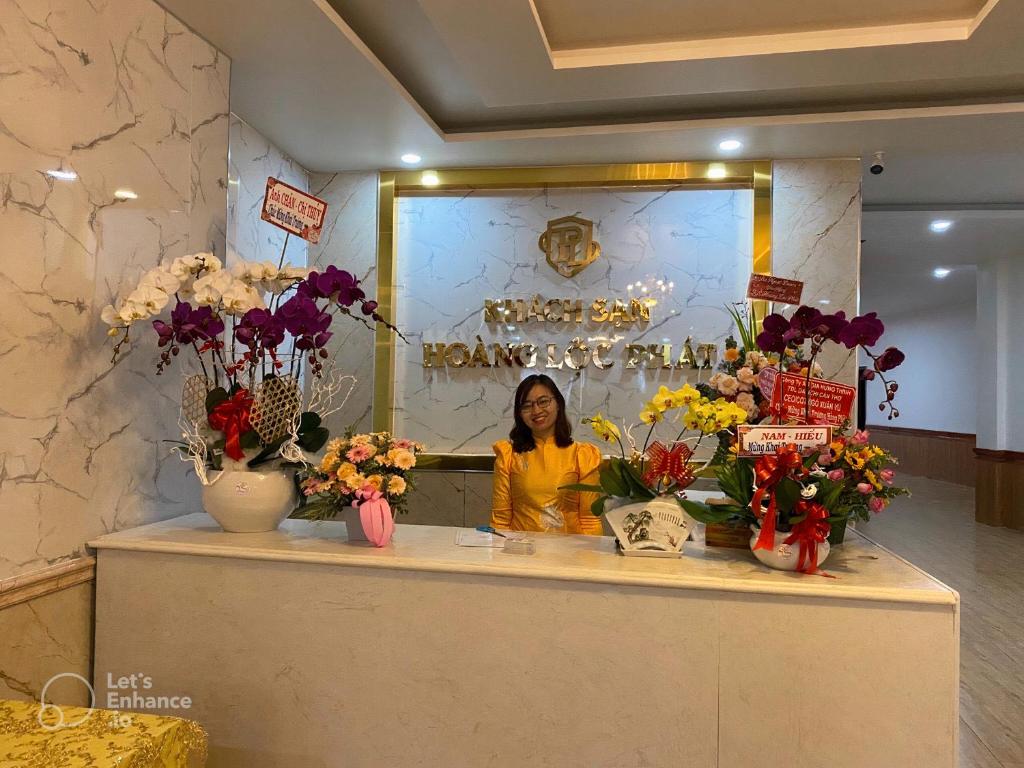 a woman standing behind a counter with flowers in vases at Hoàng Lộc Phát Hotel in Cái Răng