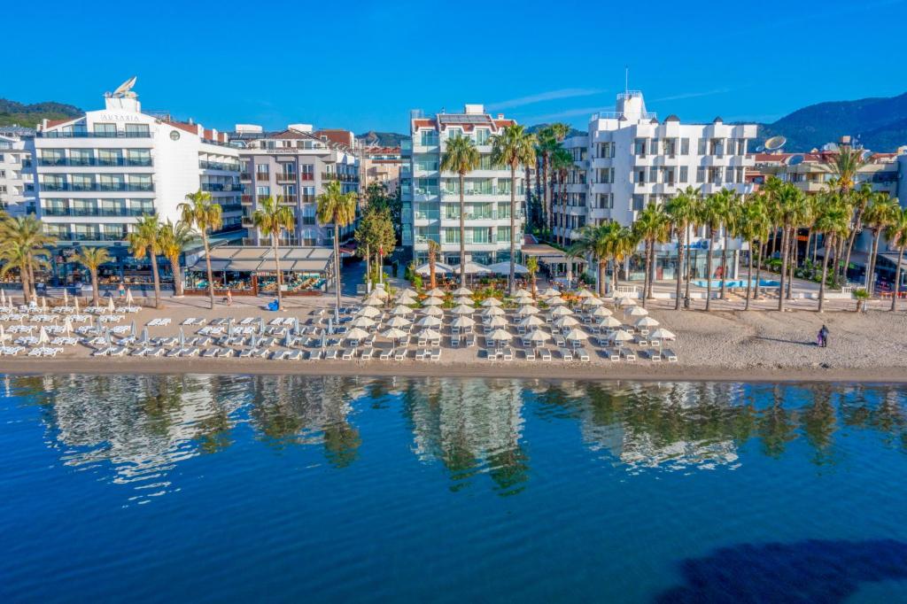 a beach with chairs and palm trees and buildings at Begonville Beach Hotel - Adult Only in Marmaris