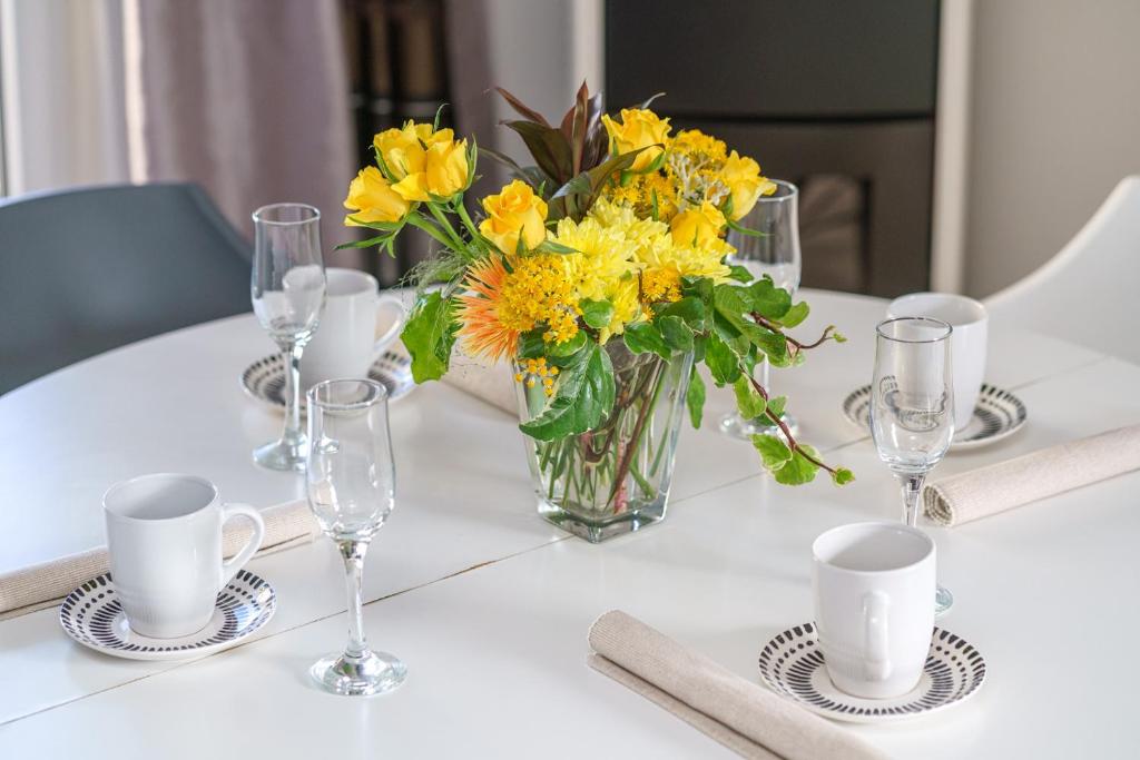 einen weißen Tisch mit einer Vase aus gelben Blumen und Gläsern in der Unterkunft Apartmani Gabriella in Vodice