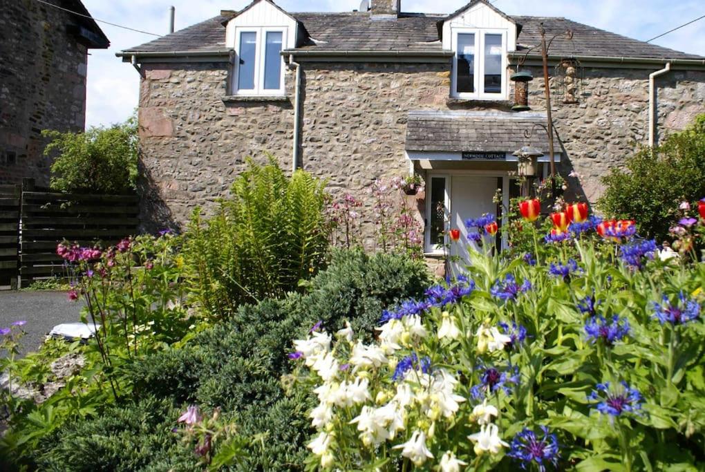 a garden in front of a stone house with flowers at Norwood Cottage in Kirkby Lonsdale