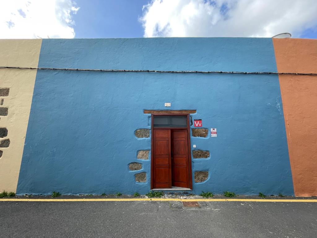 een blauwe muur met een rode deur aan de zijkant van een gebouw bij Casa Jurel in Agüimes