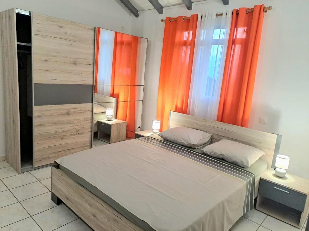 a bedroom with a large bed with orange curtains at La Familiale in Sainte-Rose