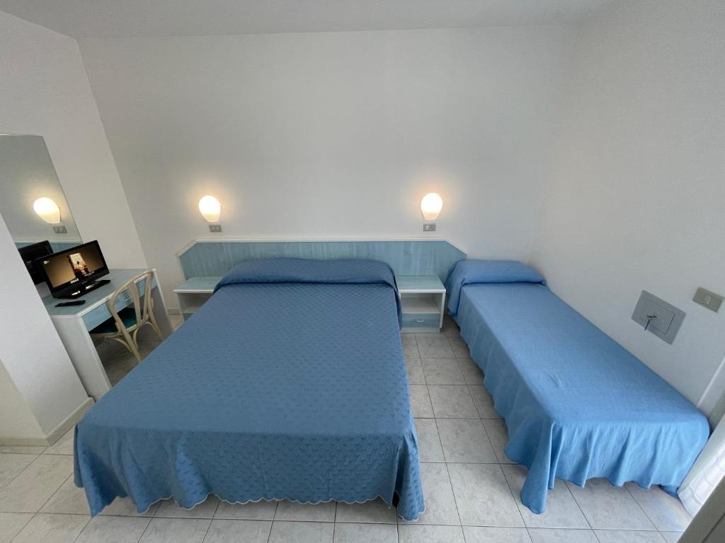 a room with two beds and a desk and a television at Albergo Désirée in Alba Adriatica