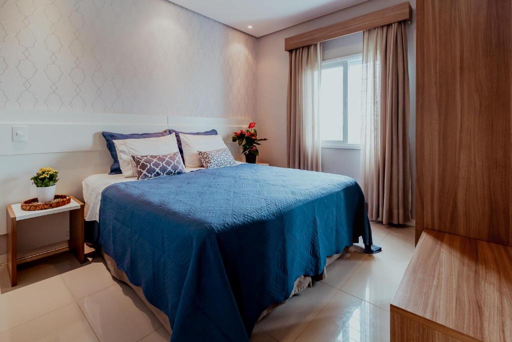 1 dormitorio con 1 cama con manta azul y ventana en Bloom Guesthouse en Holambra