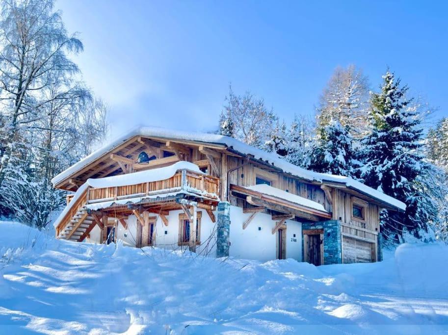 una cabaña de madera cubierta de nieve en el bosque en Chalet de luxe sur les pistes - 5 chambres, en Combloux