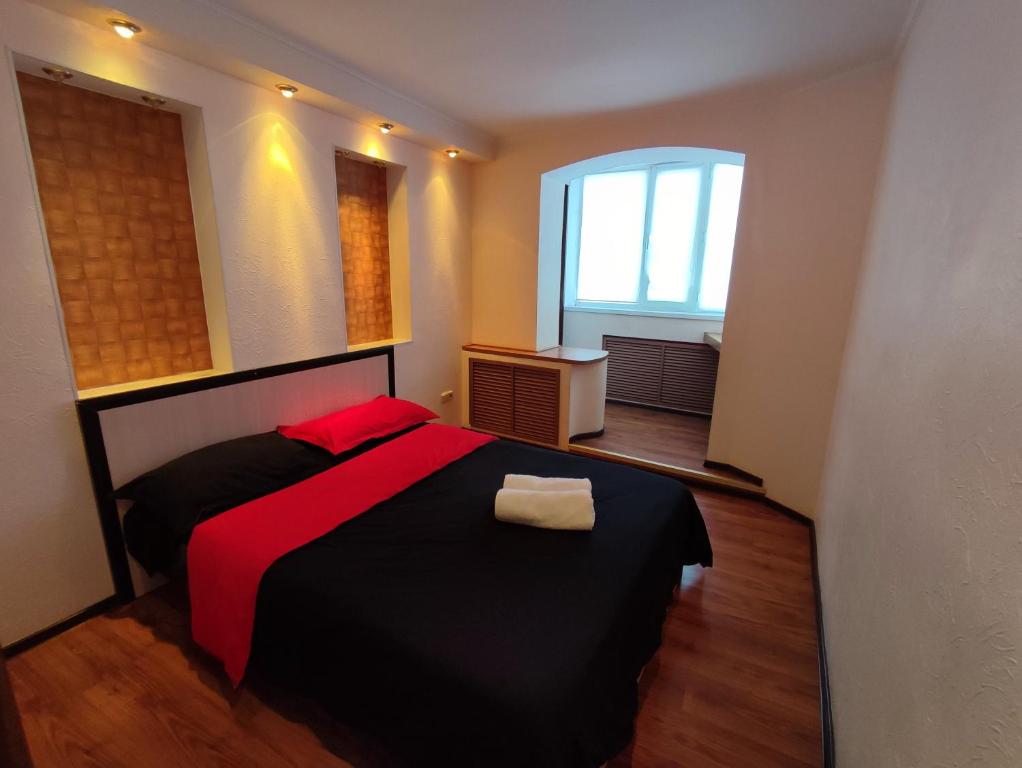 um quarto com uma cama preta com lençóis vermelhos e uma janela em Уютная трёхкомнатная квартира em Pavlodar