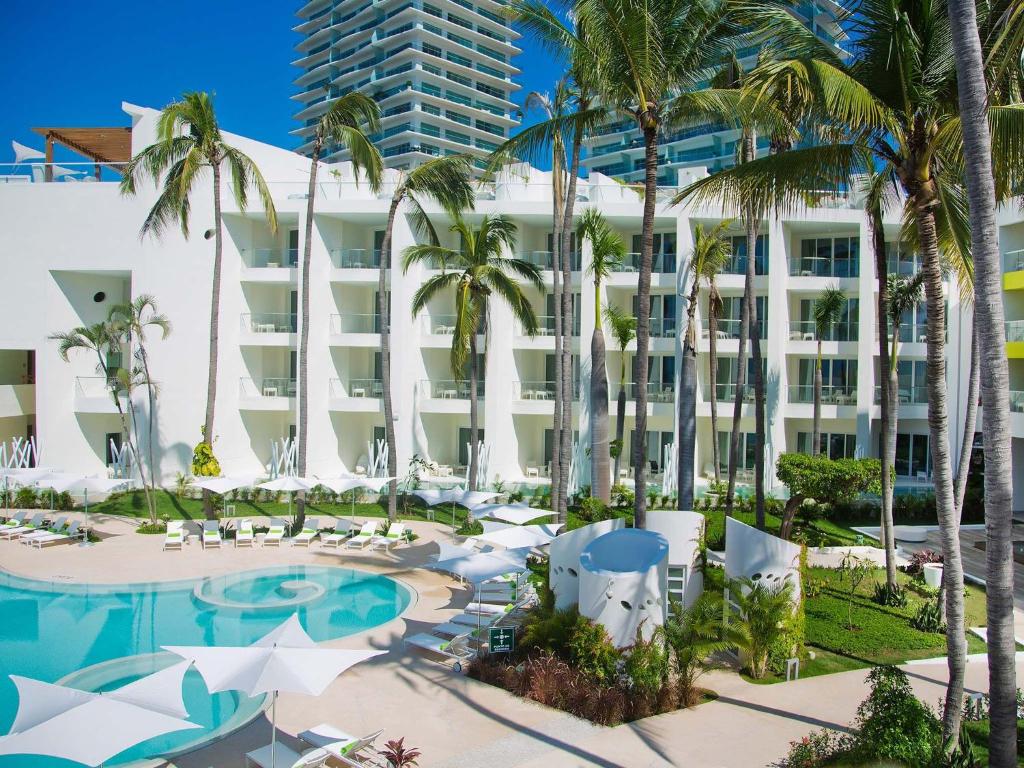 an exterior view of the resort with a pool and palm trees at Krystal Grand Puerto Vallarta - All Inclusive in Puerto Vallarta