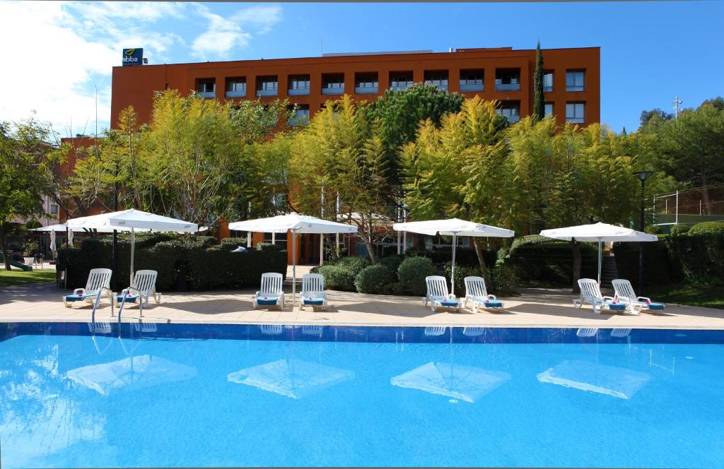 a swimming pool with chairs and umbrellas in front of a building at Abba Garden in Barcelona