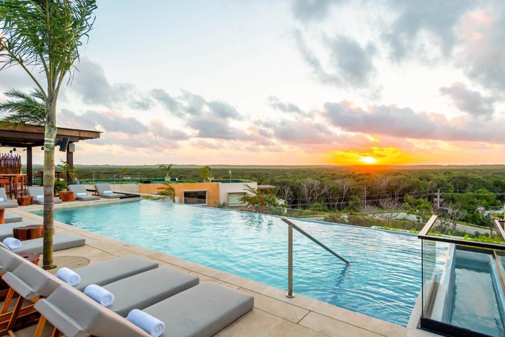 a swimming pool with chairs and a sunset in the background at Aloft Tulum in Tulum