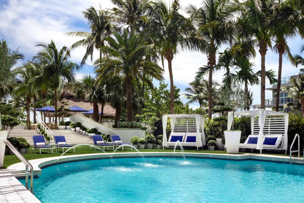 a swimming pool with chairs and palm trees at Cadillac Hotel & Beach Club, Autograph Collection in Miami Beach