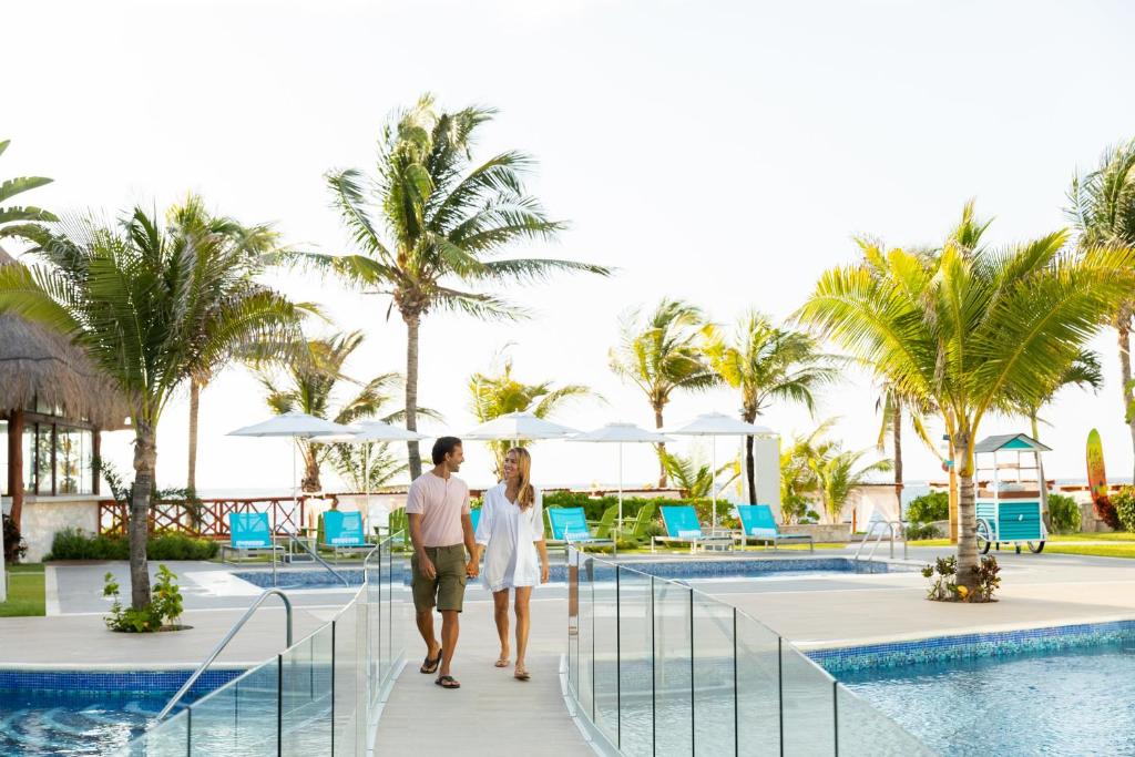 un homme et une femme se promènent au bord de la piscine d'un complexe dans l'établissement Margaritaville Island Reserve Riviera Cancún - An All-Inclusive Experience for All, à Puerto Morelos