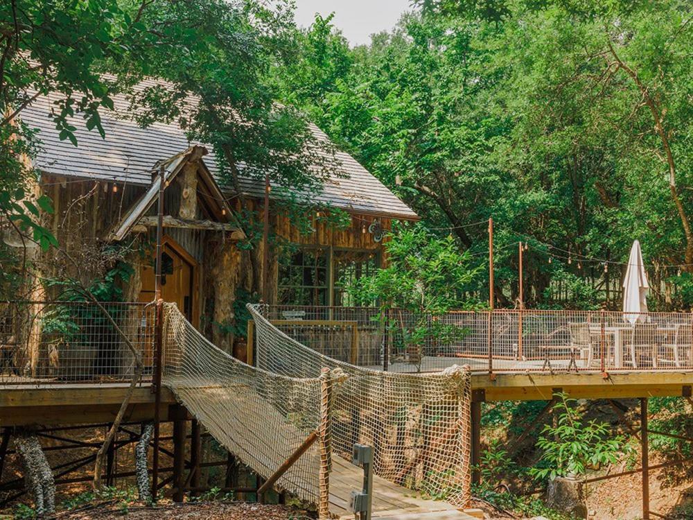 uma rede em frente a uma casa com uma ponte em Hobbit Treehouse with waterfall on the Brazos River! 350 acres! Tubing! Petting zoo! em Weatherford