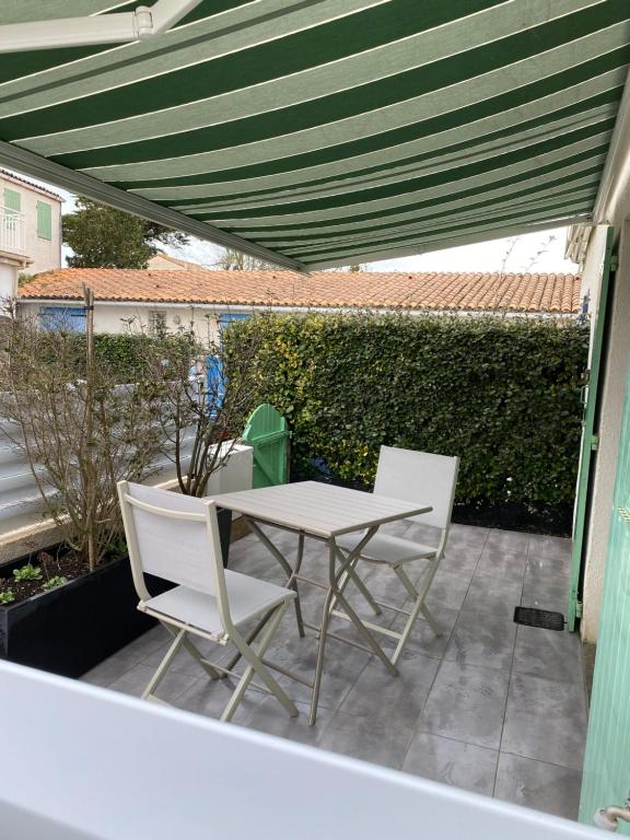 een tafel en stoelen op een patio met een groene luifel bij Au cœur de la Cotinière Studio en résidence parking privé wifi in La Cotinière