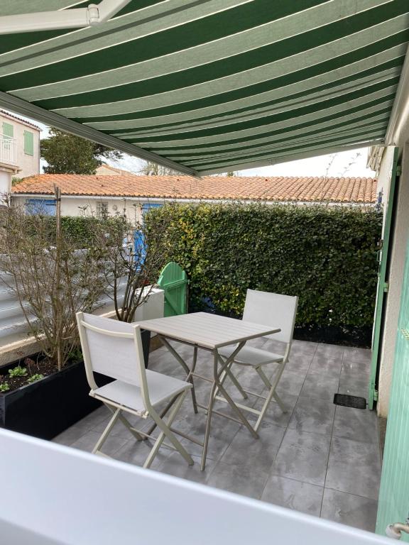 - une table et des chaises sur une terrasse avec un auvent vert dans l'établissement Au cœur de la Cotinière Studio en résidence parking privé wifi, à La Cotinière