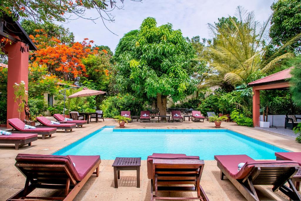 uma piscina com espreguiçadeiras e cadeiras em Hibiscus House Gambia em Brufut