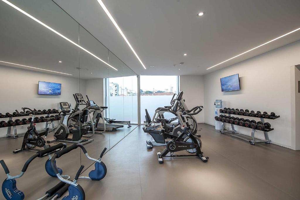 A bright, mirrored gym contains cardio machines and free weights beside large windows.