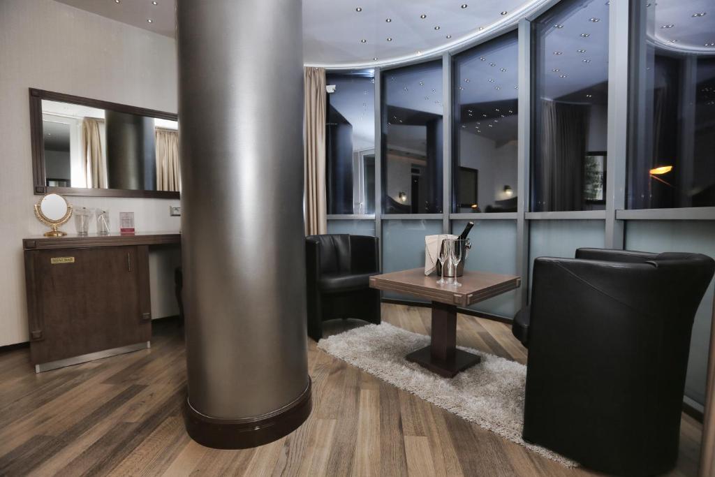 Seating area with round table, bottle of wine, two chairs, faux-fur rug and curved window with blackout blind at City Palace Hotel in Ohrid
