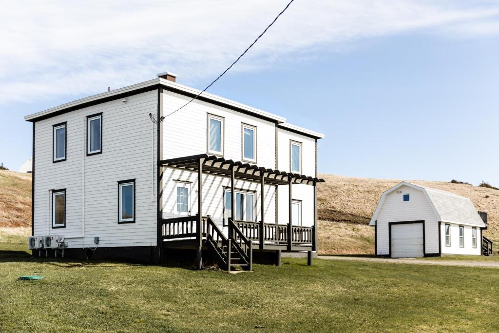 une maison blanche avec une véranda et une grange dans l'établissement Blanche de l'Ouest - Îles de la Madeleine, à Havre-Aubert