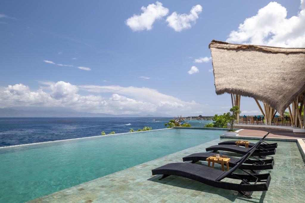 a swimming pool with lounge chairs and the ocean at Pramana Natura Nusa Penida in Nusa Penida