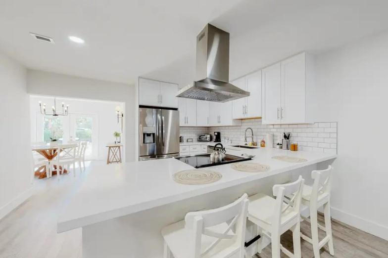 a white kitchen with a large white counter and chairs at Blue Cove in Deerfield Beach